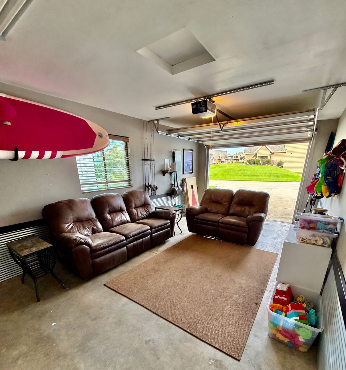 A garage with a brown leather couch, a surfboard, and a storage area with toys.