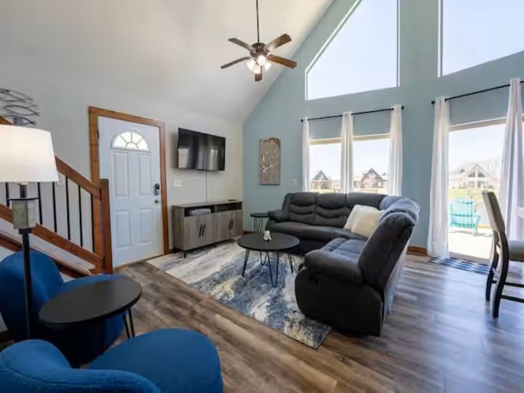A spacious living room with a sectional sofa, a ceiling fan, and a large window offering a view of the outside.