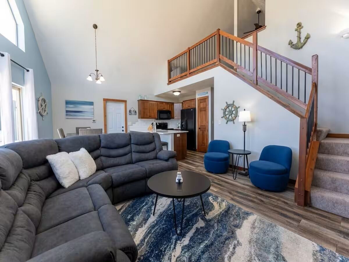 A spacious living area with a large sectional sofa, a round coffee table, and a staircase leading to an upper level.