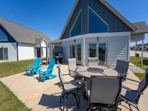 Un patio con mobiliario exterior, una parrilla y un espacio cubierto con ventanales grandes.