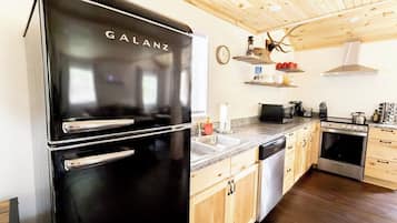 A kitchen with a black Galanz refrigerator, wooden cabinets, a microwave, and a stove.