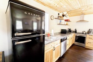 A kitchen with a black Galanz refrigerator, wooden cabinets, a microwave, and a stove.