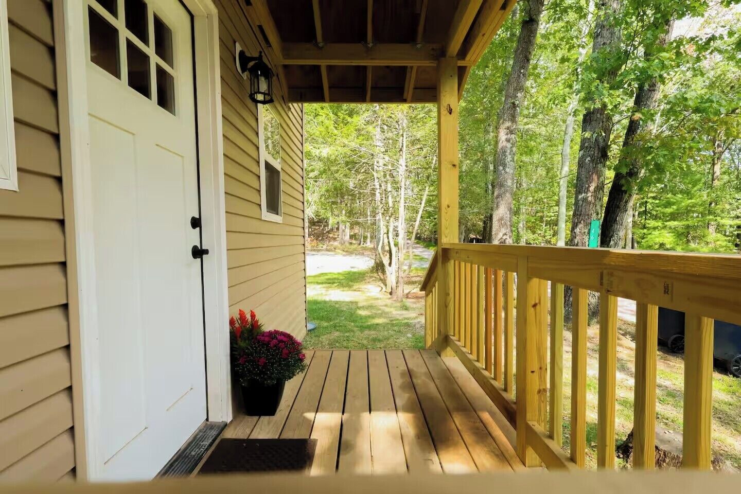 A wooden deck with a white door and a small window, surrounded by trees.