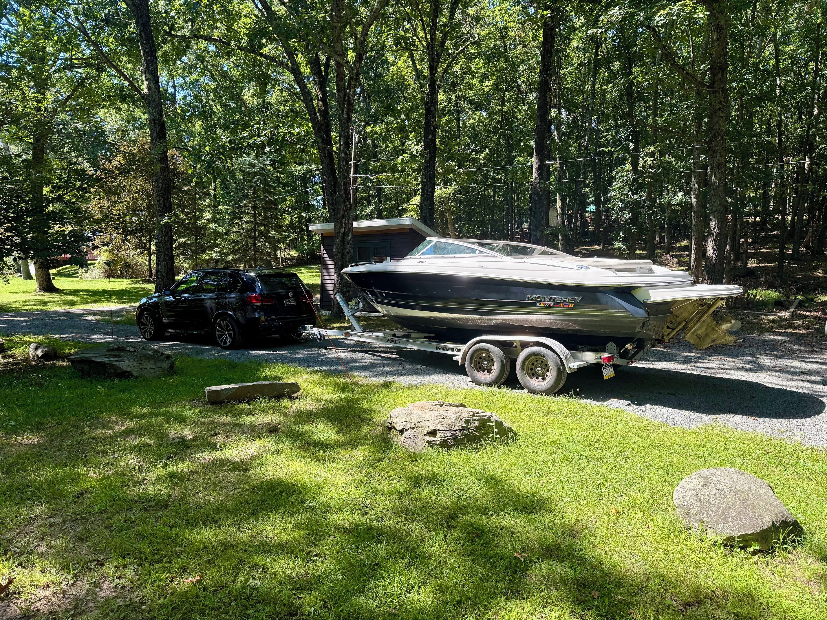 A boat on a trailer in a wooded area with a car nearby.