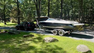 A boat on a trailer in a wooded area with a car nearby.
