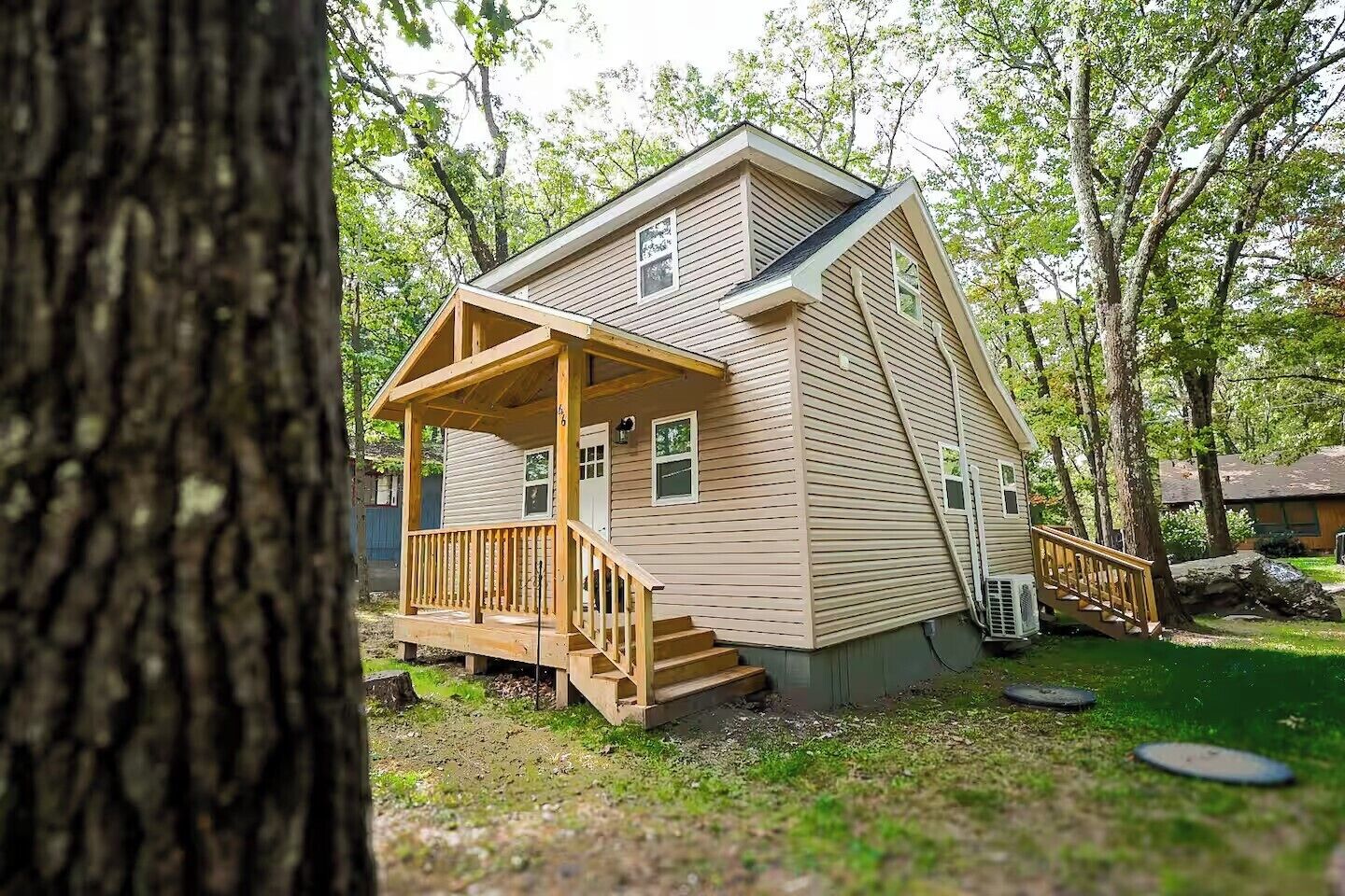 A two-story cabin with a wooden deck and a small porch, surrounded by trees.