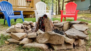 Ein Lagerfeuer, umringt von Steinen, mit drei Adirondack-Stühlen in Blau, Weiß und Rot.