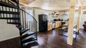 A modern kitchen with dark wood flooring, a black spiral staircase, and a dining area with wooden tables.