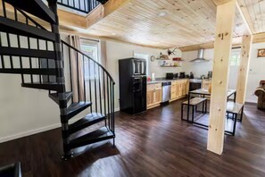 A modern kitchen with dark wood flooring, a black spiral staircase, and a dining area with wooden tables.