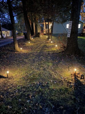 Un sendero iluminado por luces empotradas que lleva a un edificio con porche, rodeado de árboles y un letrero que indica acceso a camino privado.