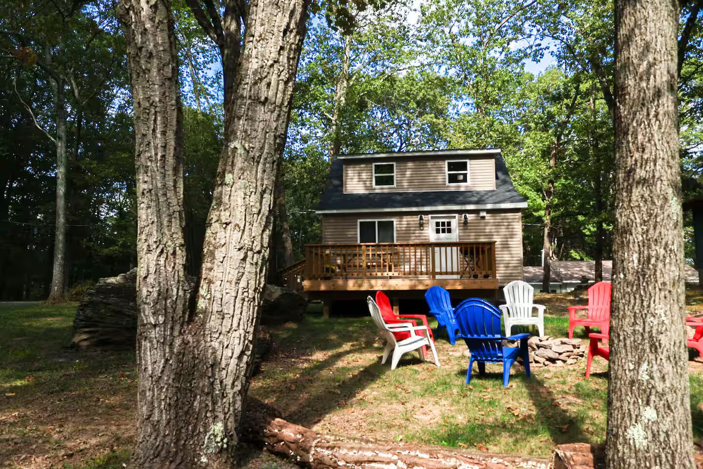 A cabin with a deck, surrounded by trees, and outdoor seating.