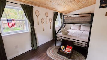 Ein Mehrbettzimmer mit Holzboden, einem Fenster mit Vorhängen und einer Wand mit Badminton-Schlägern.