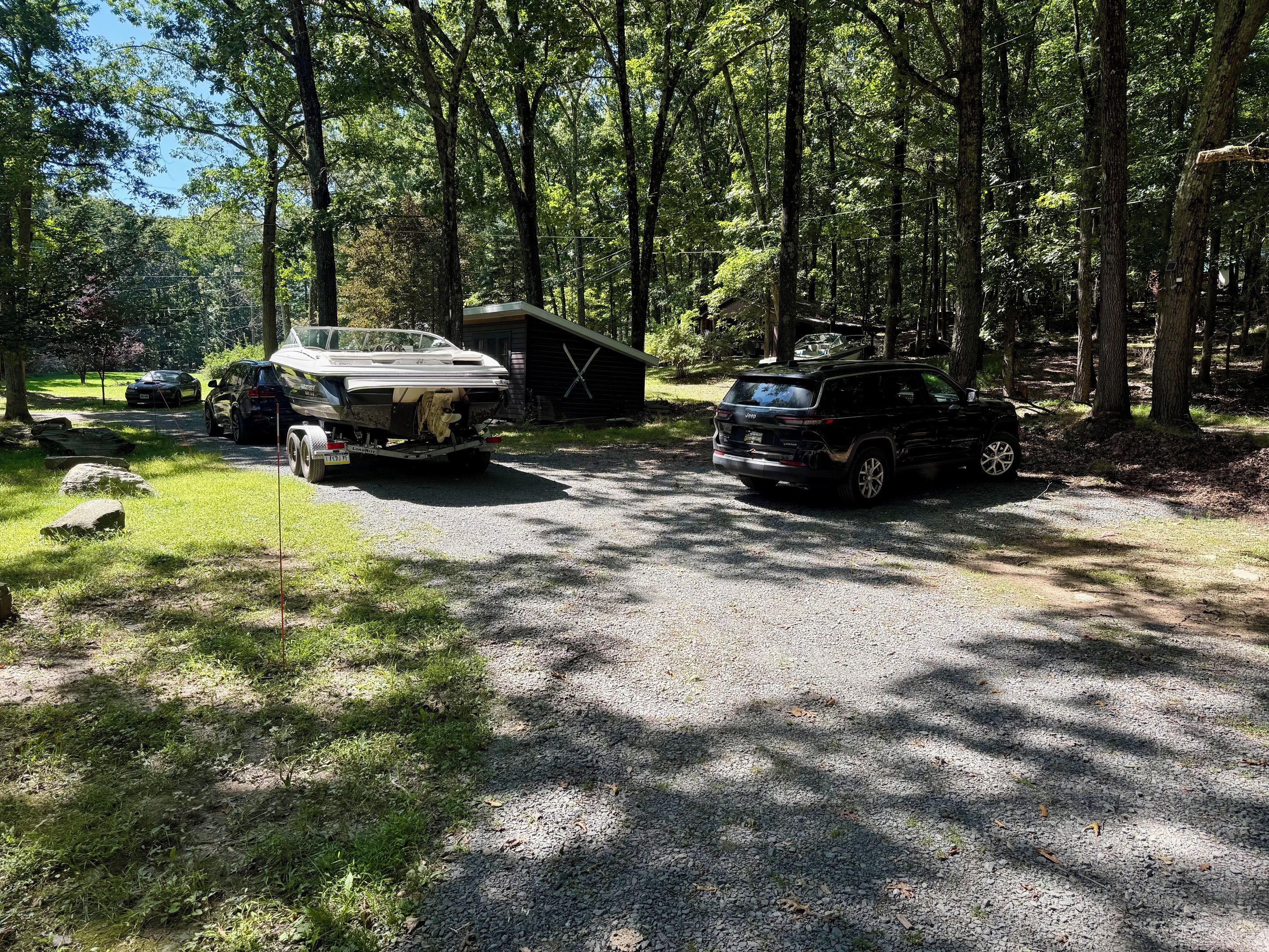 A campground with a gravel parking area, a wooden cabin, and two vehicles parked nearby.