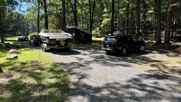 A campground with a gravel parking area, a wooden cabin, and two vehicles parked nearby.
