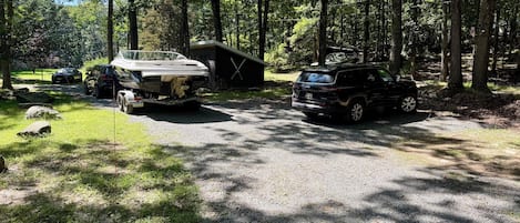 A campground with a gravel parking area, a wooden cabin, and two vehicles parked nearby.