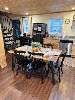 Una cocina moderna con un refrigerador negro, armarios de madera, un lavavajillas de acero inoxidable y un comedor con una mesa de madera y sillas negras.