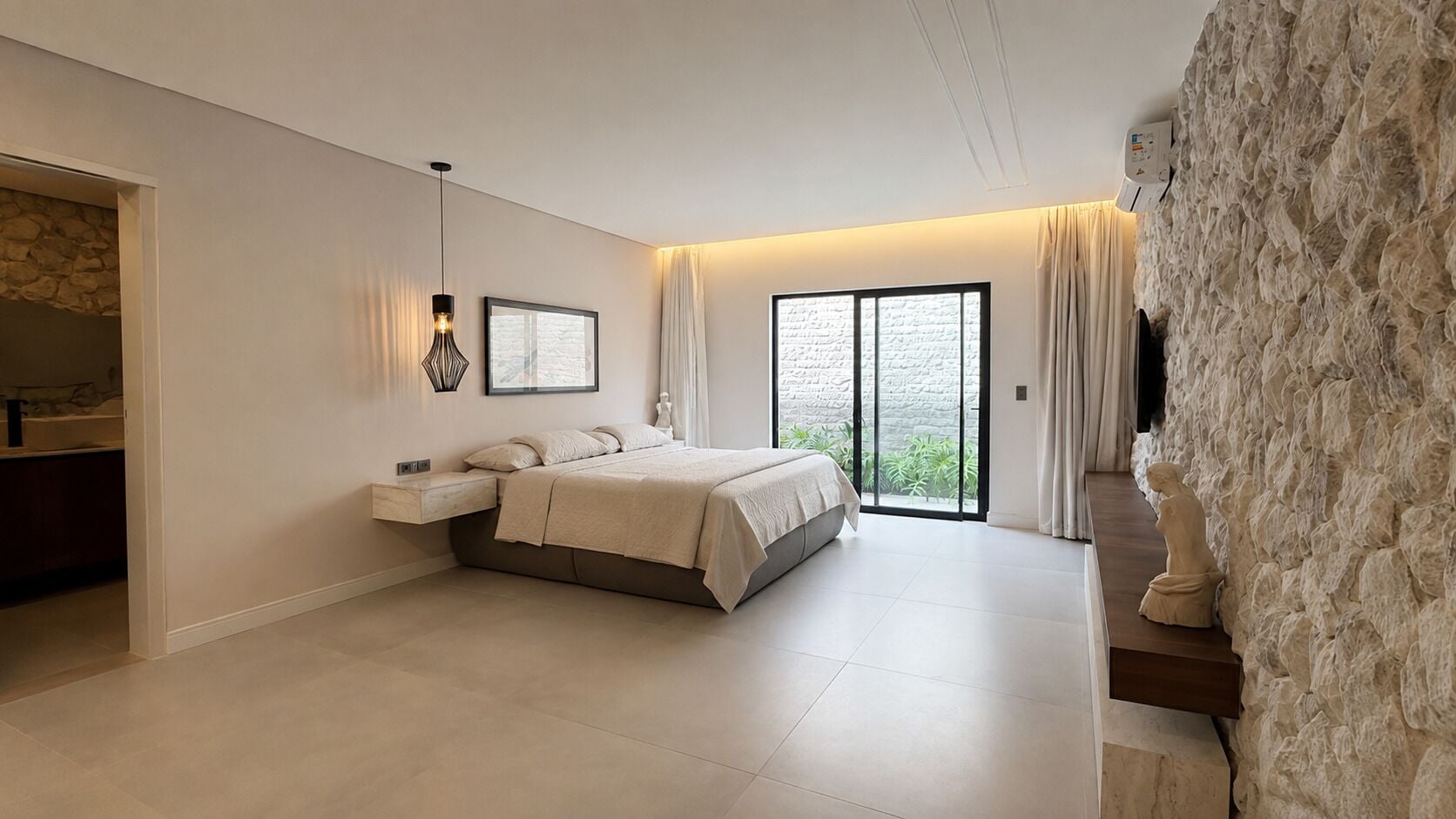 A modern bedroom with a large bed, a nightstand, a wall-mounted light, and a view through a glass door.