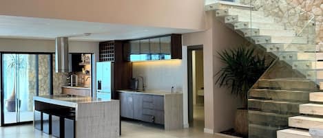A spacious living area with a modern kitchen, a stone accent wall, and a glass staircase.