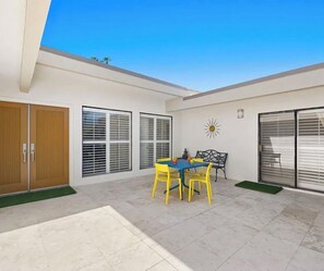 A patio with a table and chairs, a sliding door, and a wall-mounted sun decoration. - Spacious 3-bedroom condo in a resort like community in Indian Wells. (Indian Wells)