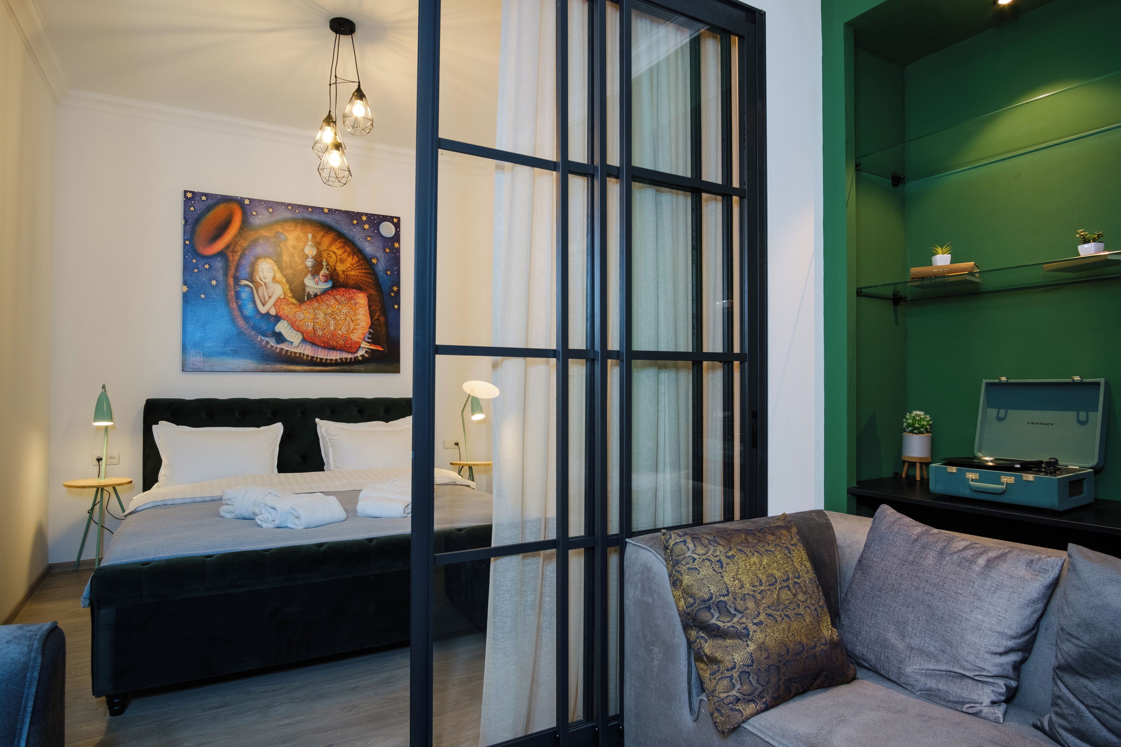 A modern bedroom with a bed, a sofa, a painting, a desk with a computer, and a green wall.