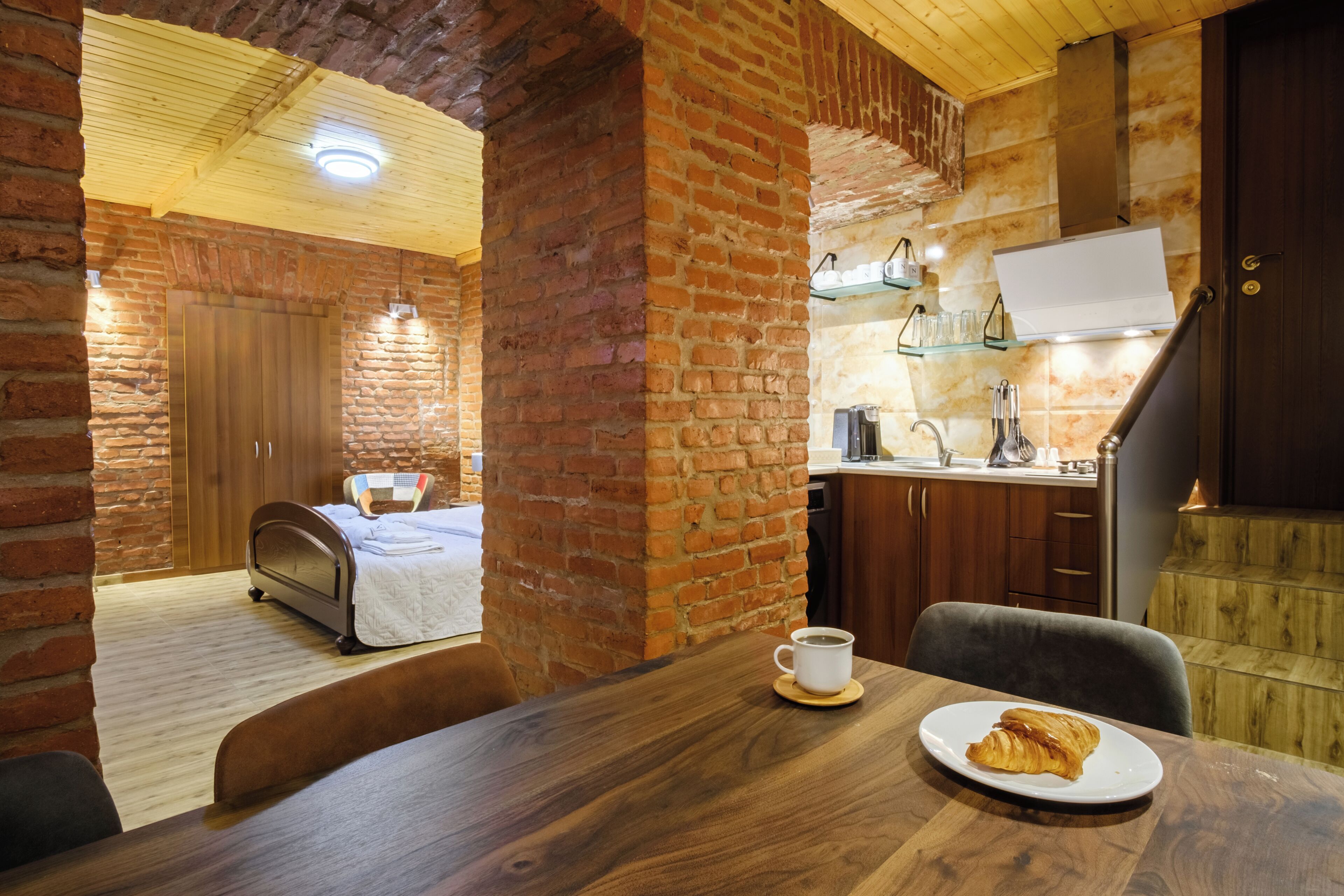 A cozy room with a bed, a dining table with a plate of food, and a kitchen area with a sink and cabinets.
