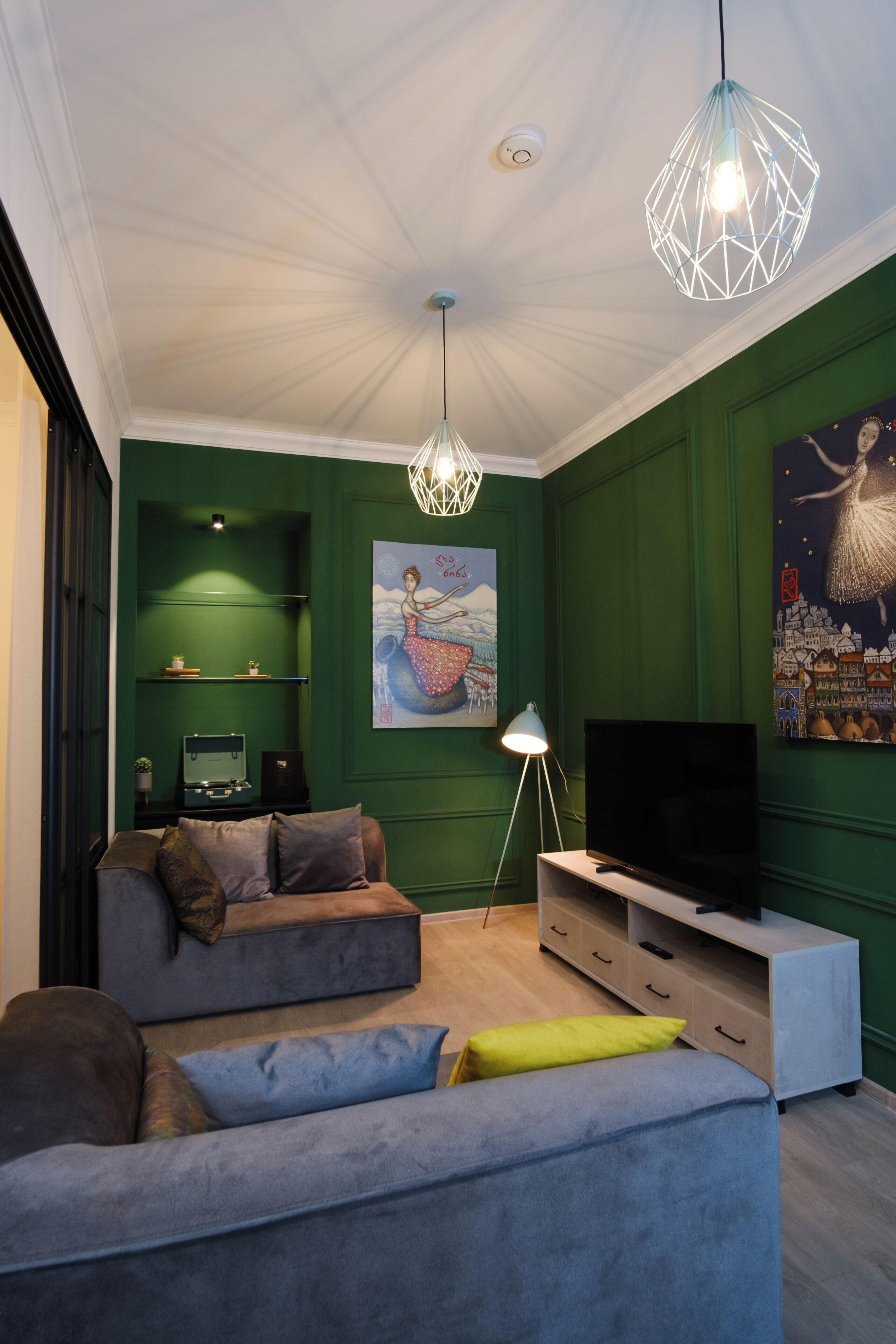 A modern living room with a green wall, a large painting, a sofa, a TV, and a unique geometric light fixture.