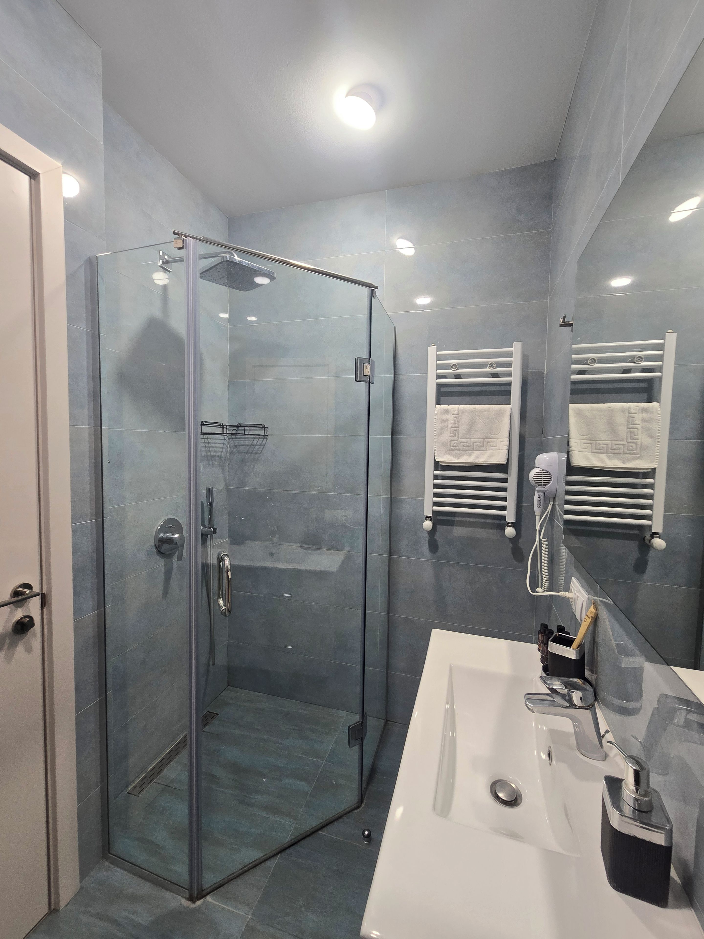 A modern bathroom with a glass-enclosed shower, a white sink, and towel racks.