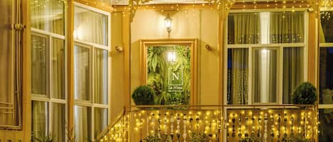 A building facade with multiple windows, a balcony with string lights, and a poster with greenery.