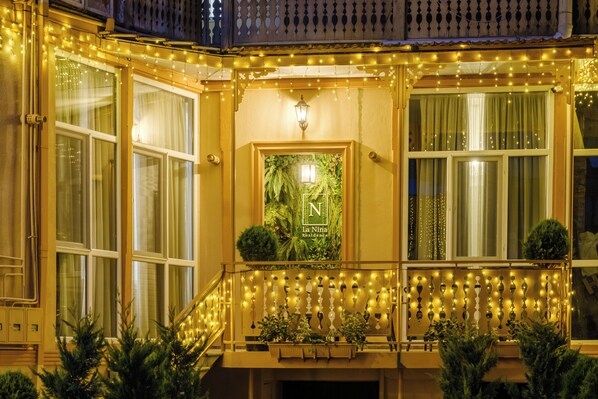A building facade with multiple windows, a balcony with string lights, and a poster with greenery.