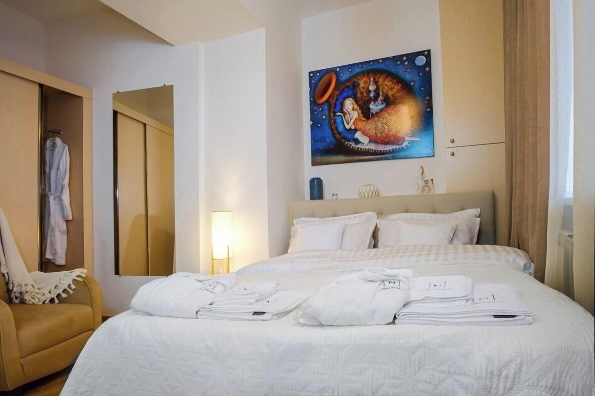 A hotel room with a bed, a chair, a painting, and a wardrobe.
