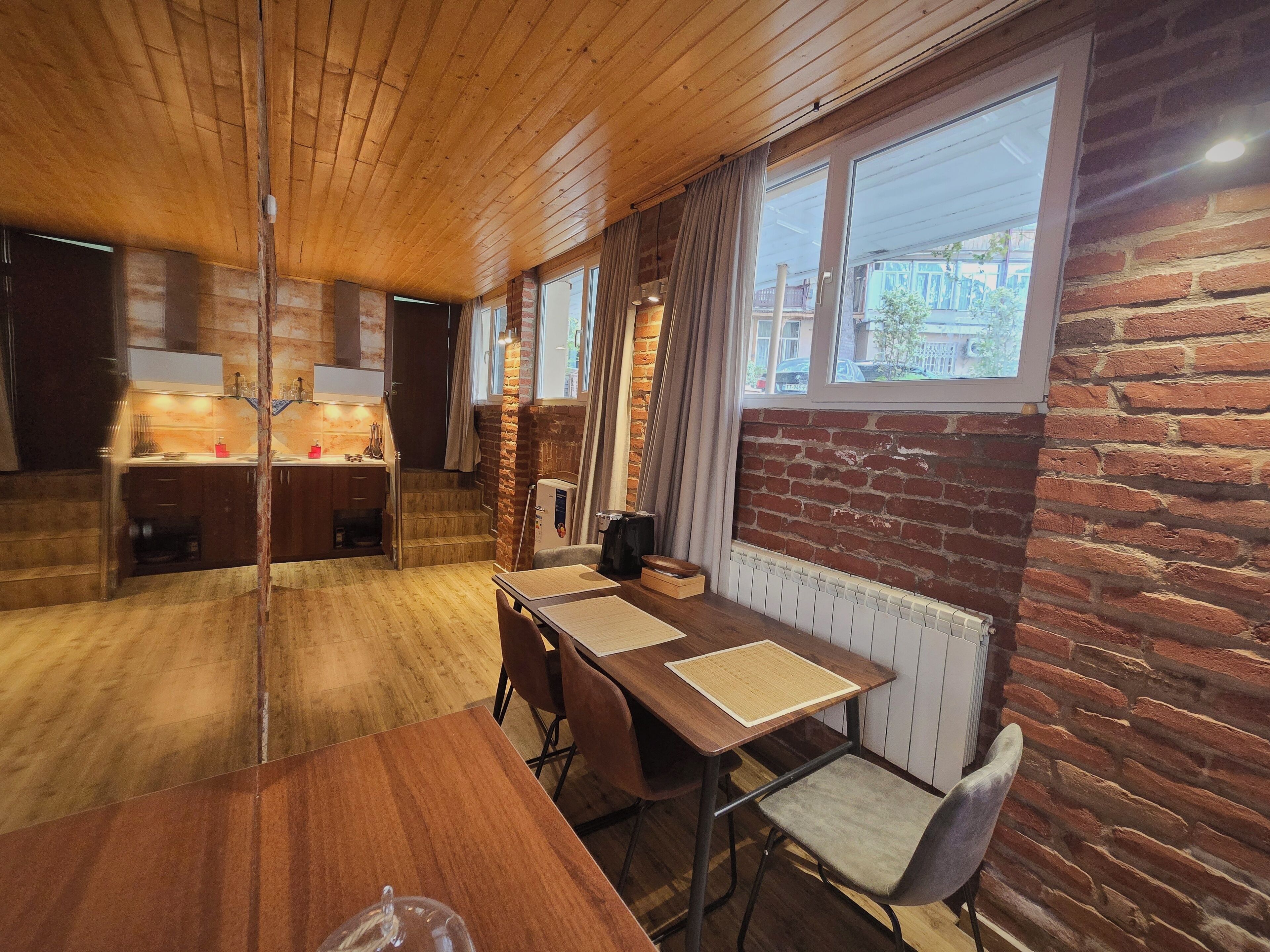 Una habitación con techo de madera, paredes de ladrillo, una mesa de comedor con sillas y una ventana con cortinas.