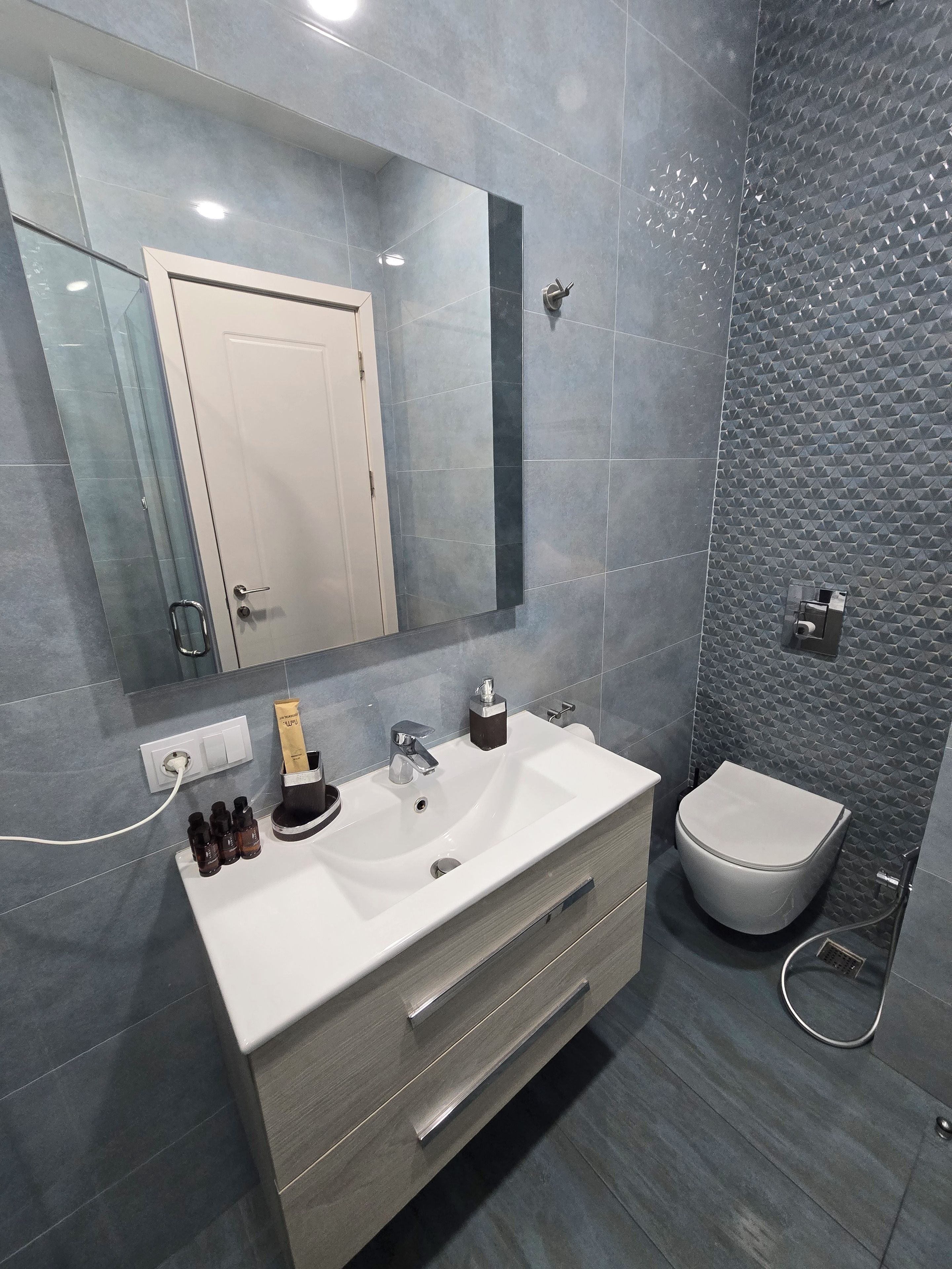 Une salle de bain moderne avec un meuble-lavabo blanc, un grand miroir et des toilettes.