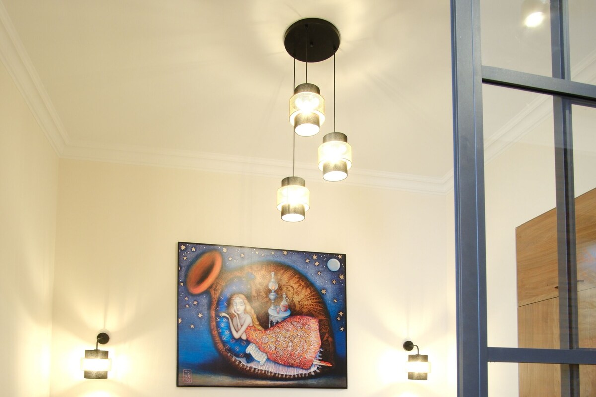 A bedroom with a bed, bedside tables, a painting, and pendant lighting.