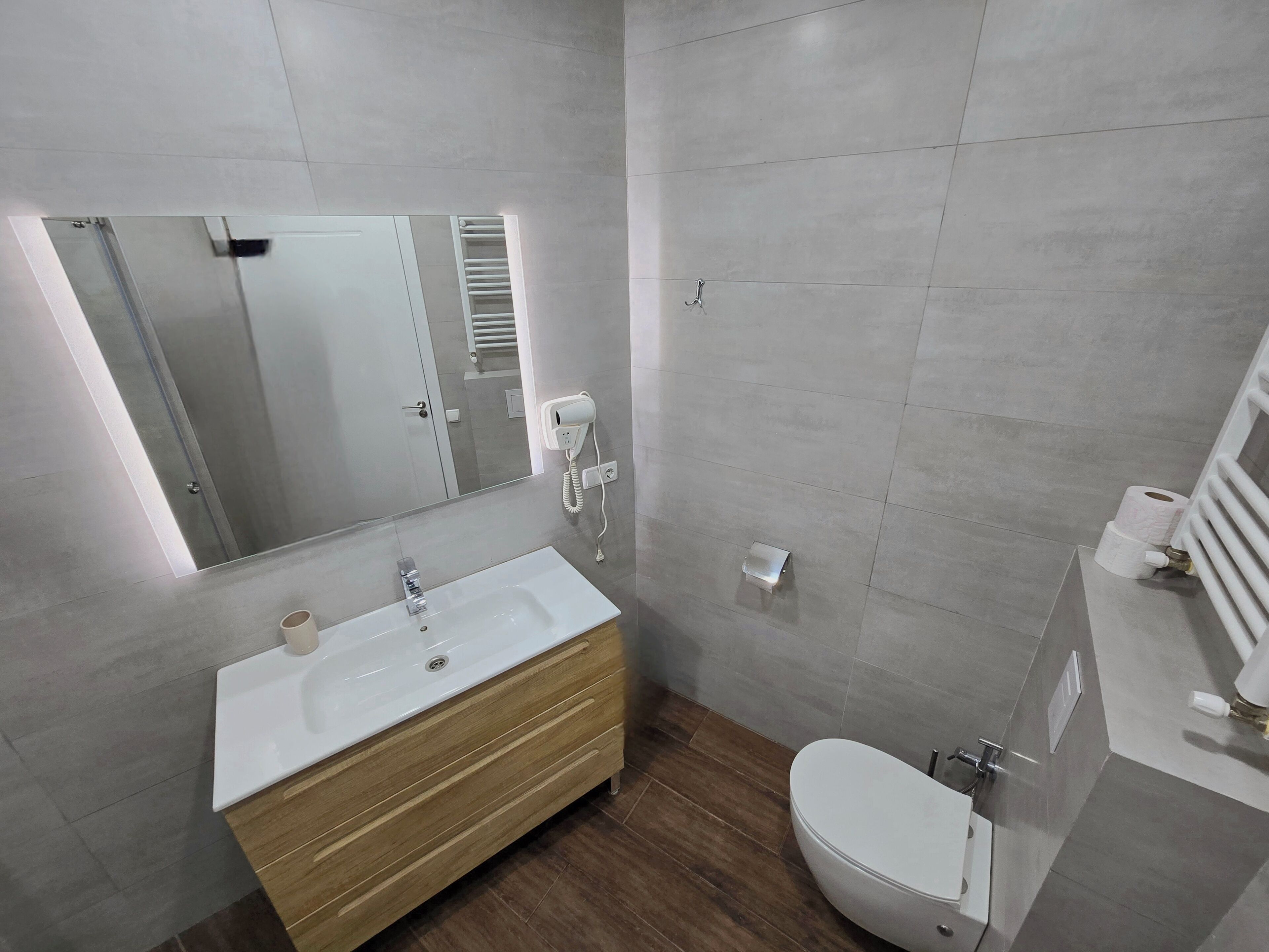 Une salle de bain moderne avec un lavabo blanc, un meuble-lavabo en bois, des toilettes et un grand miroir.