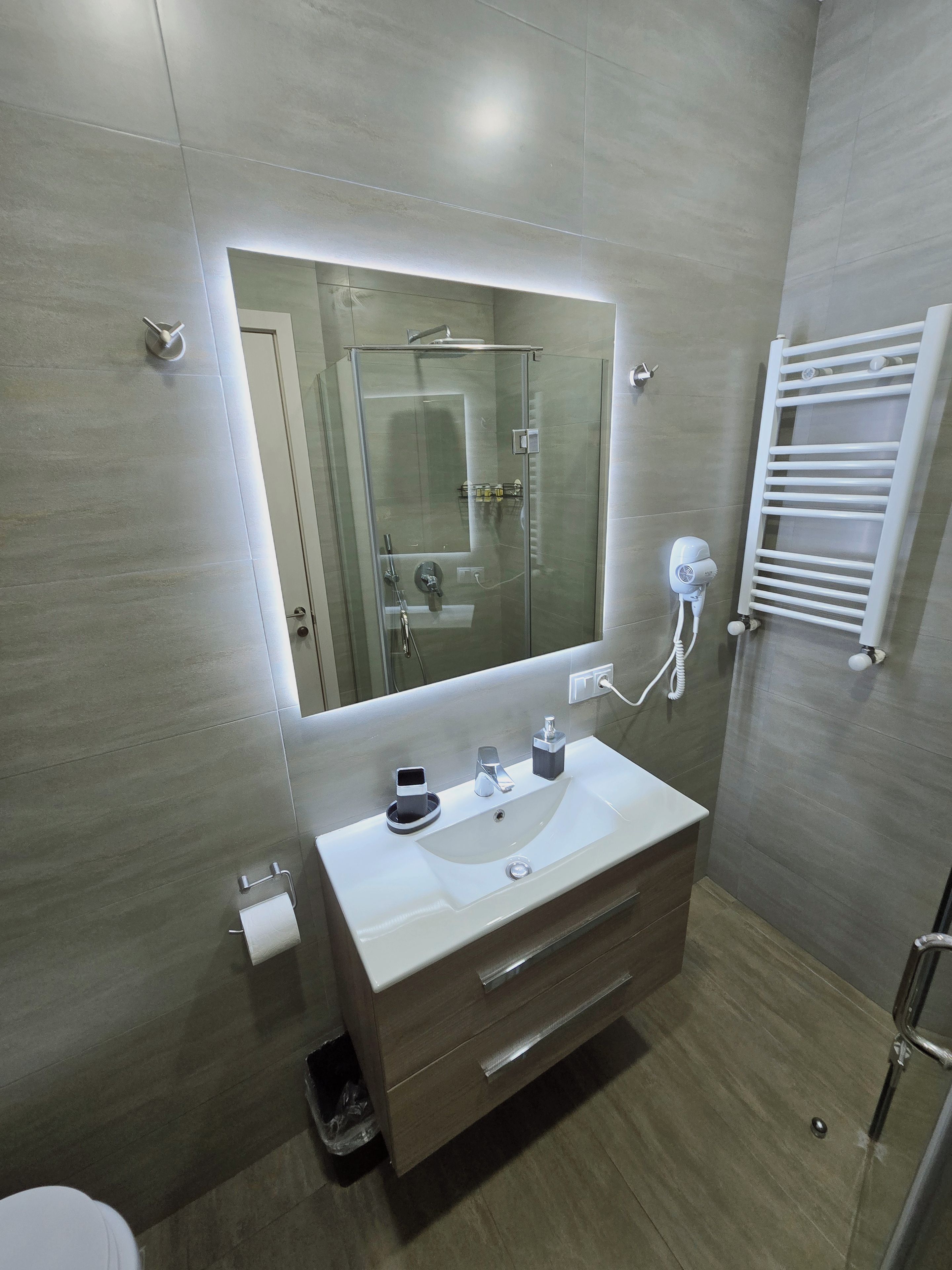 Une salle de bain moderne avec une douche à parois de verre, un lavabo blanc avec un miroir au-dessus et un porte-serviettes fixé au mur.