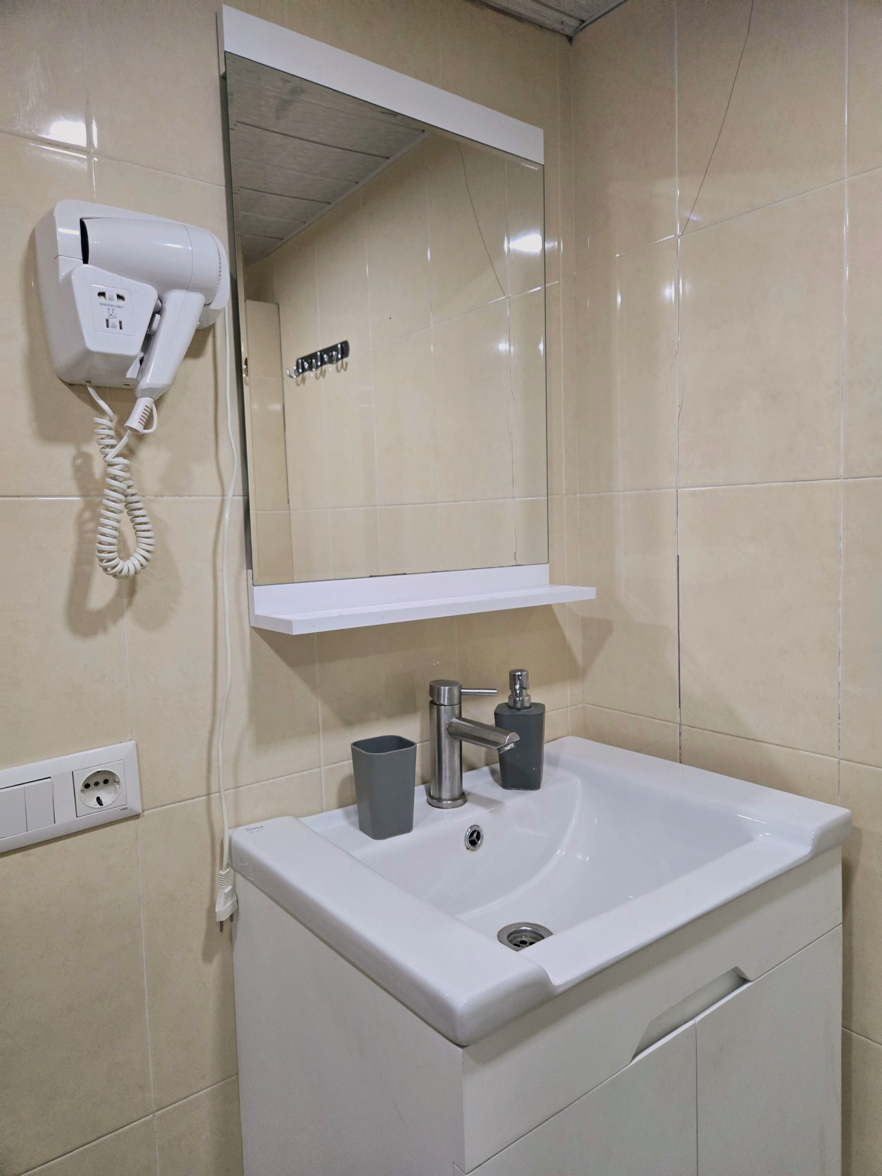 A bathroom with a white sink, a mirror, a hairdryer, and a shelf.