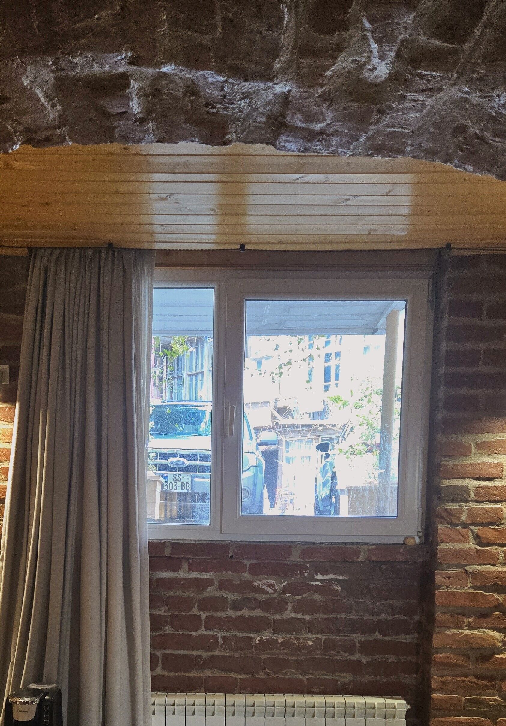 A room with a window, wooden beams, and a brick wall.