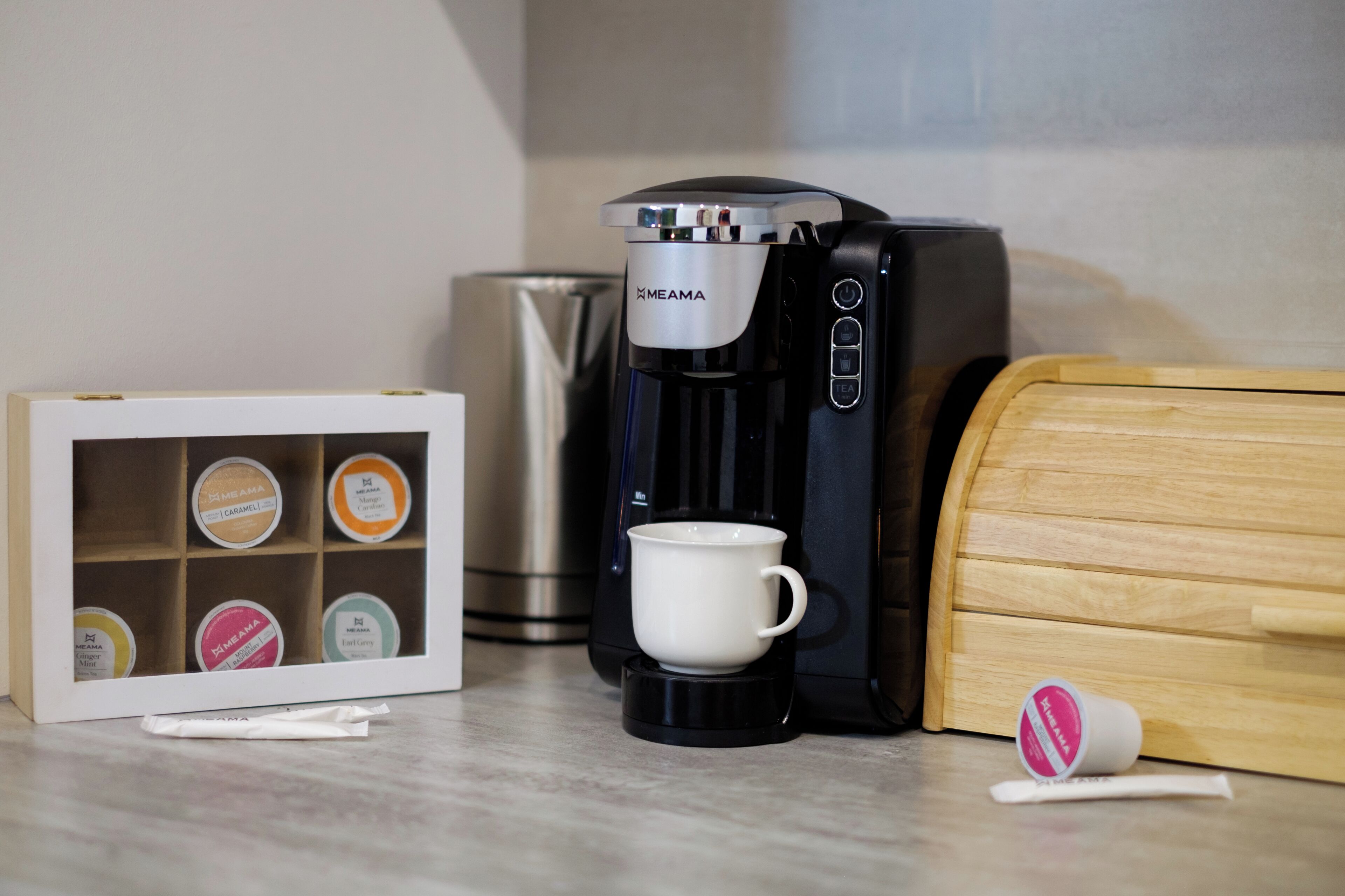 Une machine à café, une tasse et une boîte de dosettes de thé sur un plan de travail.