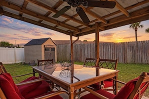 An outdoor patio with a table and chairs, a ceiling fan, and a wooden fence in the background. - Beach Bungalow Near Ormond Beach and the Atlantic (Ormond Beach)