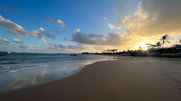 A beach with a calm sea, a clear sky, and a sunset.