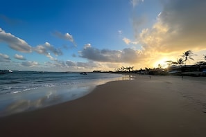 Una playa con un mar tranquilo, cielo despejado y un atardecer.
