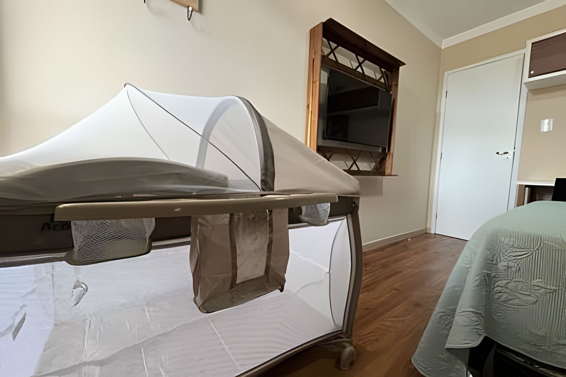 Uma cama de hospital num quarto com chão de madeira, uma janela com moldura de madeira e uma porta.