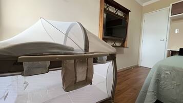 Uma cama de hospital num quarto com chão de madeira, uma janela com moldura de madeira e uma porta.