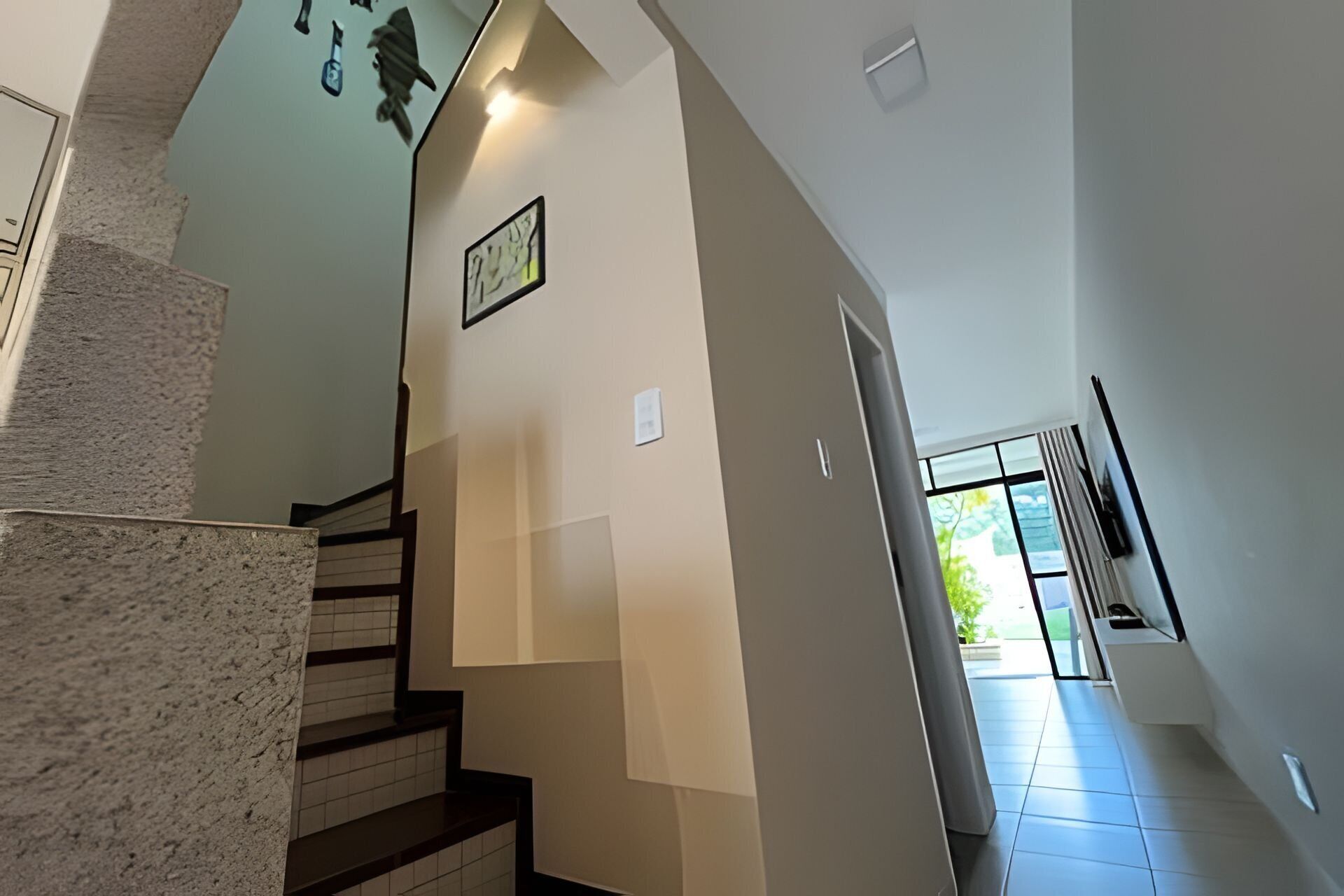 Una escalera con barandilla, un cuadro colgado en la pared y una puerta que da a una habitación luminosa con vistas.
