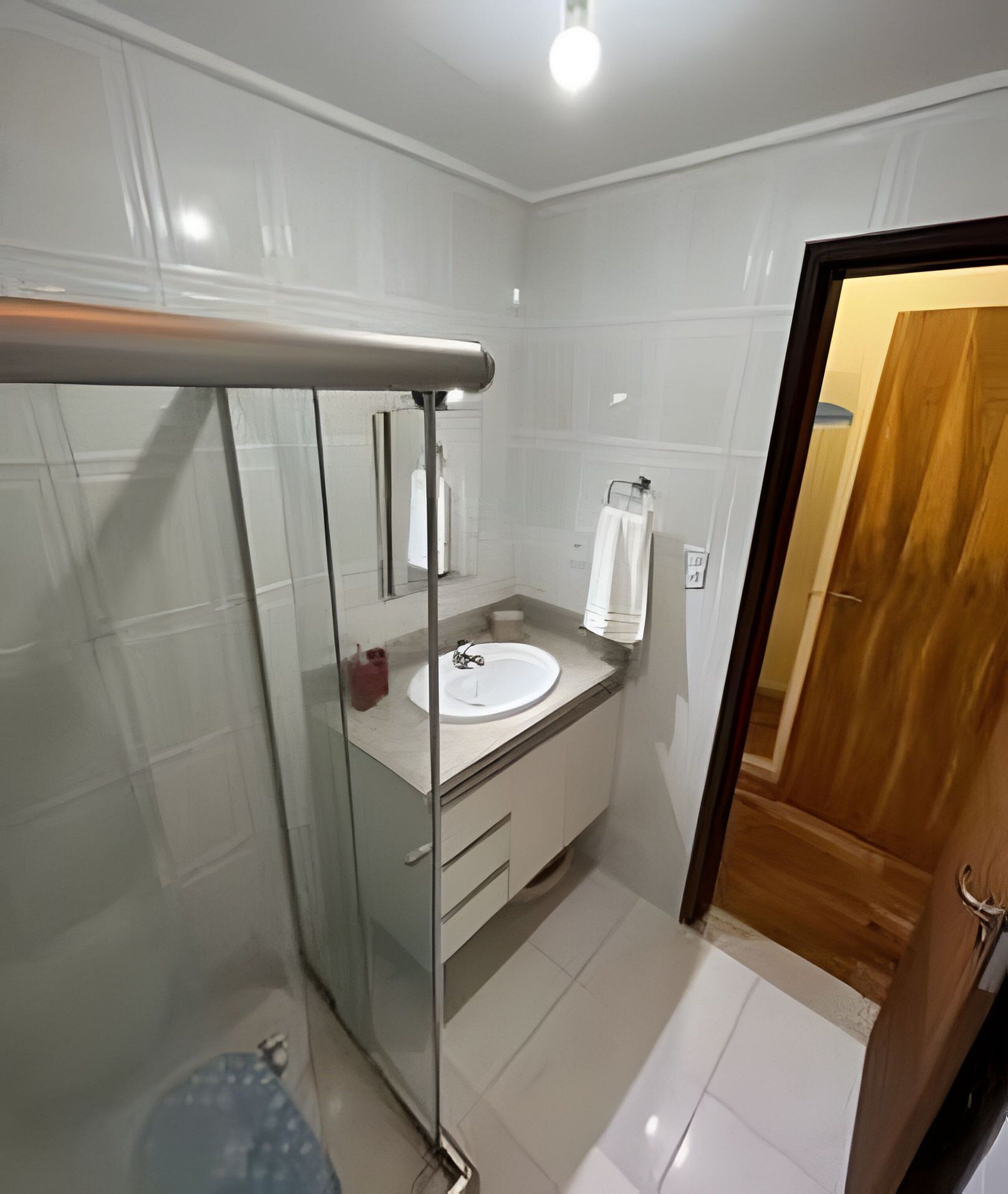 A bathroom with a glass shower enclosure, a white sink, and a wooden door.