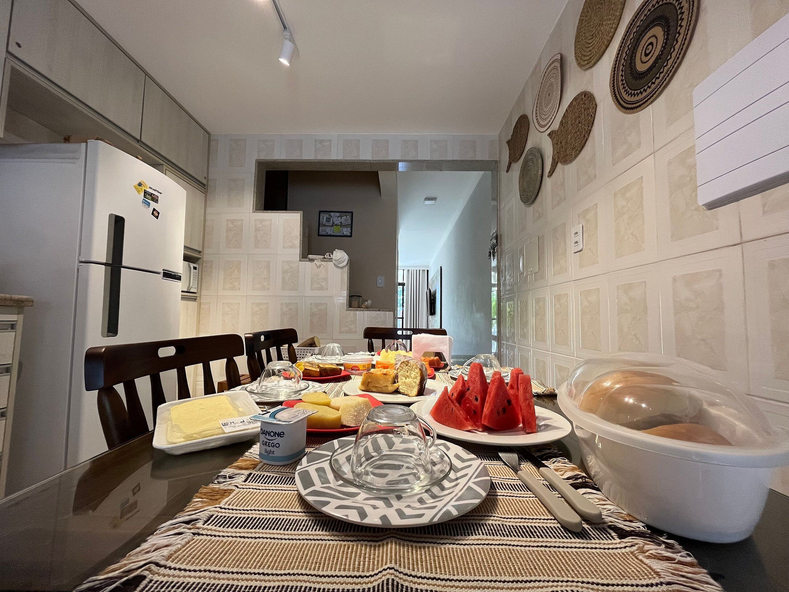 Una cocina con una mesa de comedor lista para una comida, que incluye diversos alimentos y un refrigerador.