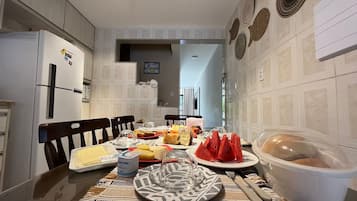 Una cocina con una mesa de comedor lista para una comida, que incluye diversos alimentos y un refrigerador.