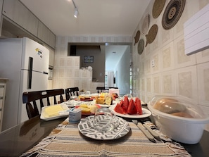 Una cocina con una mesa de comedor lista para una comida, que incluye diversos alimentos y un refrigerador.