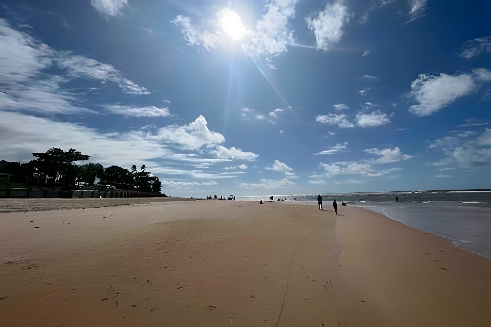 Una playa con cielo despejado, algunas personas caminando y un mar tranquilo.