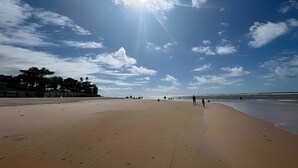 Una playa con cielo despejado, algunas personas caminando y un mar tranquilo.